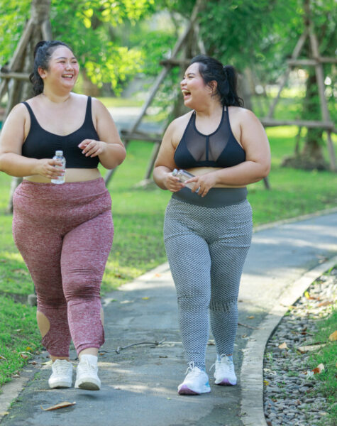 Cheerful two women overweight in sportswear have fun exercising in garden. Asian girls plus size wear sports uniform are friend together running exercise in green public park, healthy concept.
